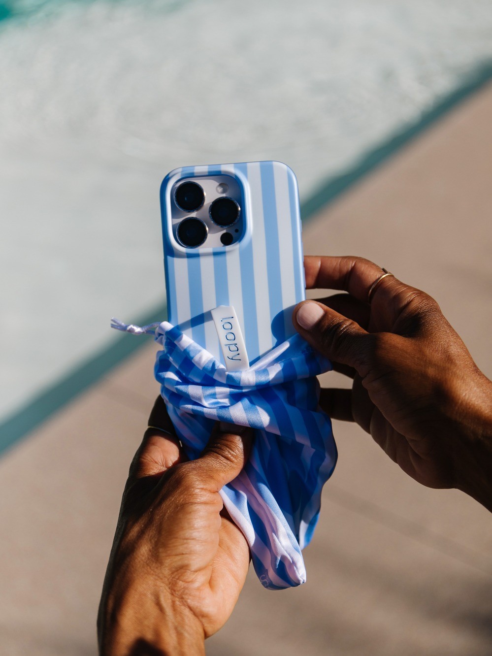 Publicité Facebook lifestyle de Loopy Cases pour une coque de téléphone à rayures bleues, tenue au bord d'une piscine