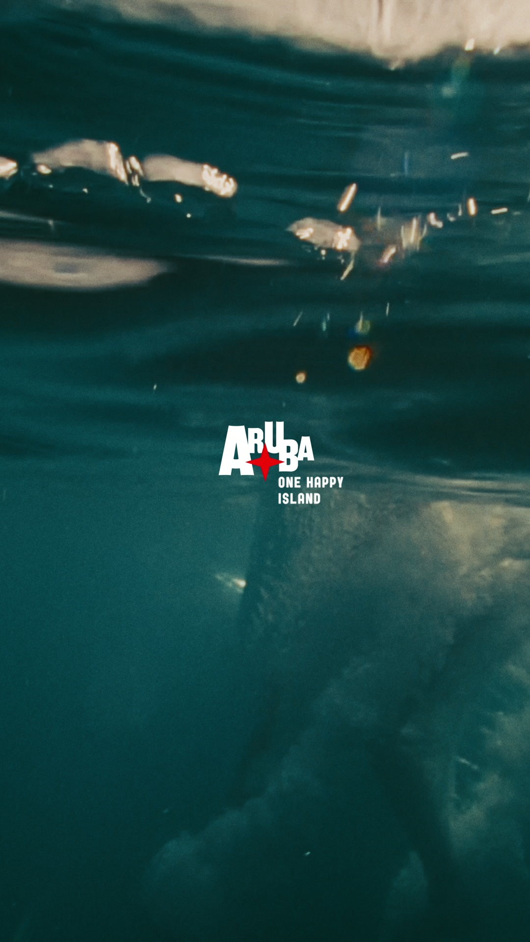 Aruba destination video ad, underwater shot of sunlit turquoise sea with the Aruba One Happy Island logo centered
