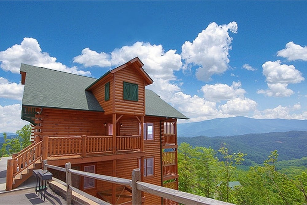 Visit My Smokies ad, a large wooden log cabin on a ridge overlooking the forested Smoky Mountains under a blue sky